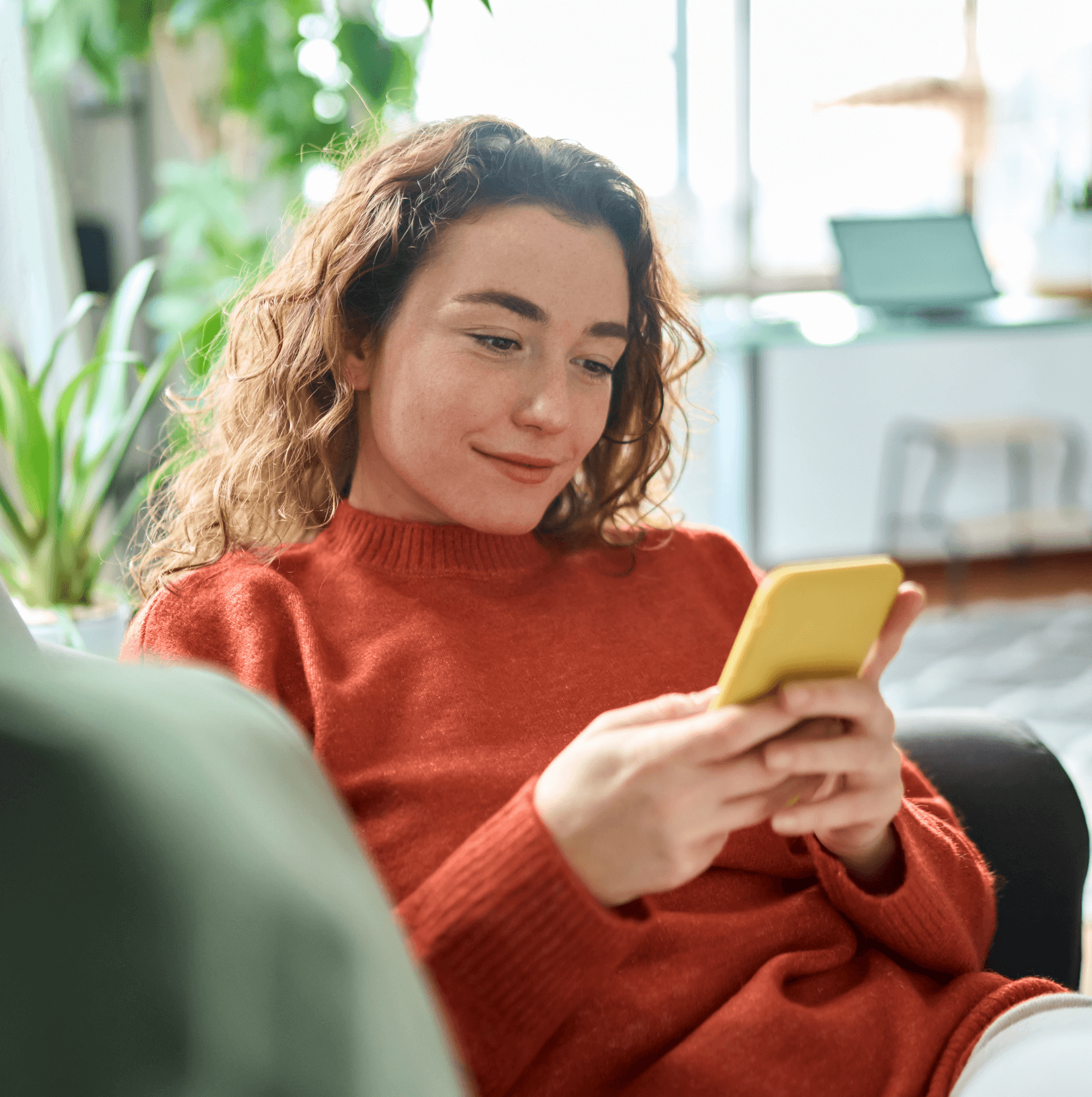A person in a red sweater holding a yellow smartphone, seated on a sofa.